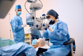 A female ophthalmologist is examining a senior female patient through a microscope during eye surgery.