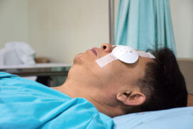 A man is sleeping and using an eye shield after eye surgery to correct his vision in the hospital room.