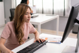 Asian female employee having farsighted problem looking at monitor