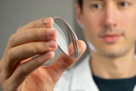 Young man doctor holds a round crystal glass lens for eyeglasses in his hand